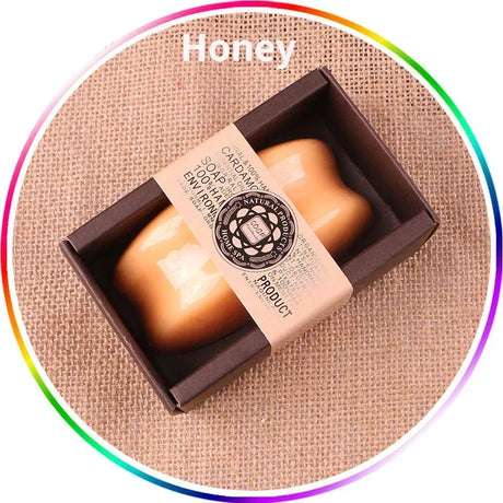 Honey-colored soap bar in a box with a visible brand label on a textured beige background.
