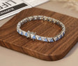 Silver bracelet with blue gemstones on a wooden surface, branded 'Orsa Jewels'.