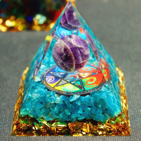 Pyramid-shaped crystal with colorful interior and gold base on a gray surface