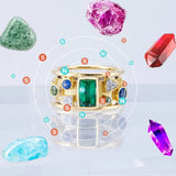 Gold ring with gemstones surrounded by various colored crystals on a light blue background