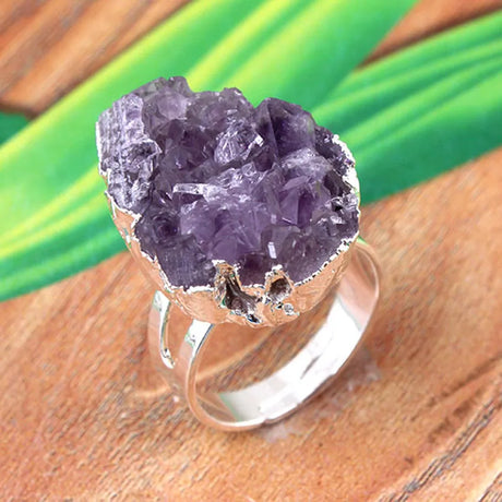Amethyst crystal ring on a wooden surface with green leaves in the background