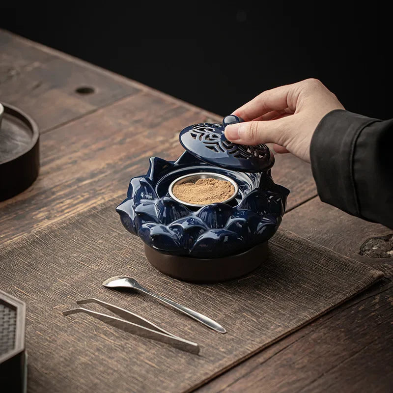 Person opening a blue ceramic container on a wooden table with tea-making tools.