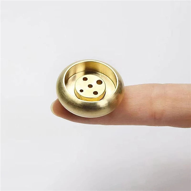 Gold-colored decorative object held between fingers on a white background