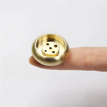 Gold-colored decorative object held between fingers on a white background