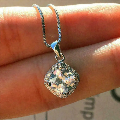 Silver necklace with a diamond pendant held between fingers