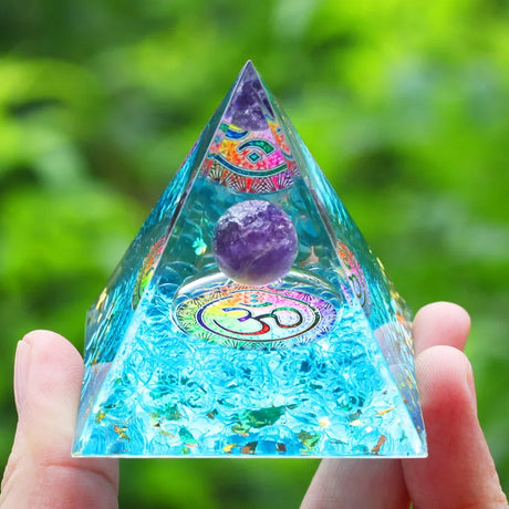 Pyramid-shaped crystal with OM symbol held by a hand against a green blurred background