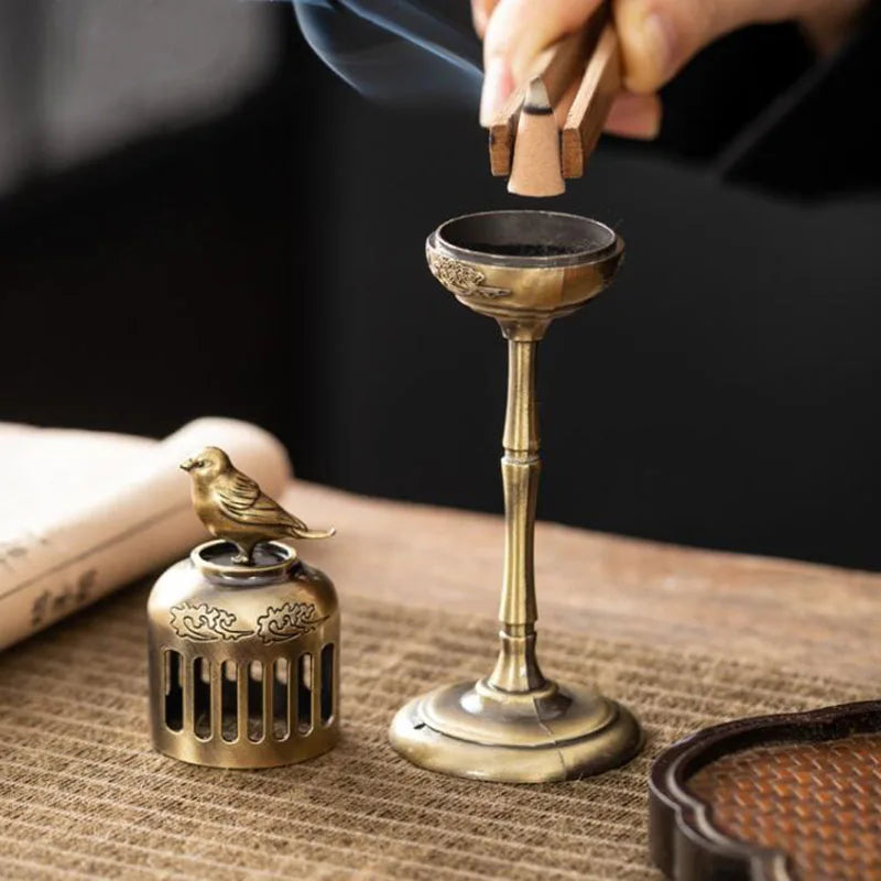 Bronze incense burner with a small bird ornament on a textured surface.