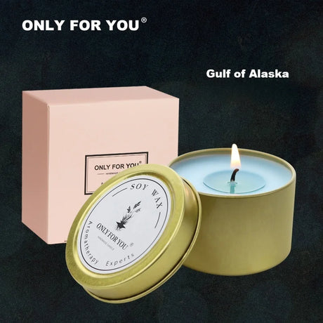 Candle in a green tin with a lit wick, next to a pink box, on a dark background.