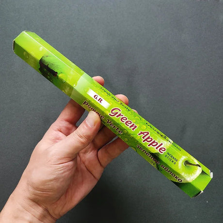 Hand holding a green box labeled 'Green Apple' against a dark background