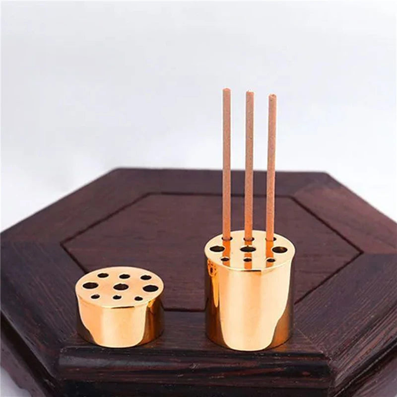 Gold incense holder with three sticks on a wooden surface