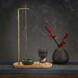 Incense burner with incense stick, small Buddha statue, and vase with red flowers on a dark background