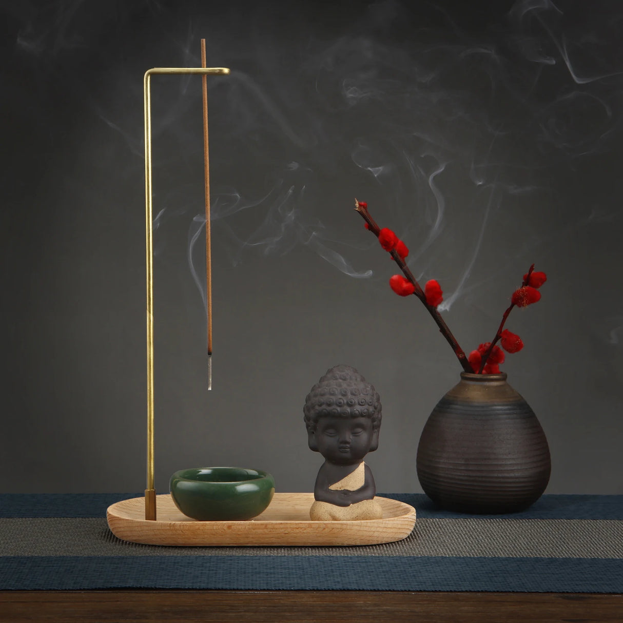 Incense burner with incense stick, small Buddha statue, and vase with red flowers on a dark background