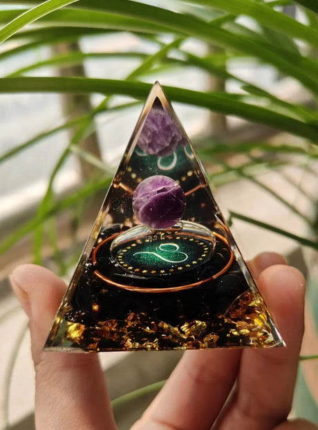 Triangular crystal with purple crystals and green design held by a hand with a blurred plant background