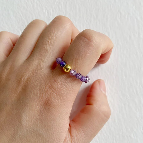 Hand wearing a ring with purple and gold beads on a white background