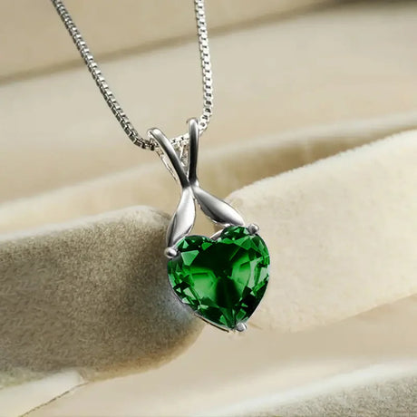 Green heart-shaped gemstone pendant on a silver chain against a beige background