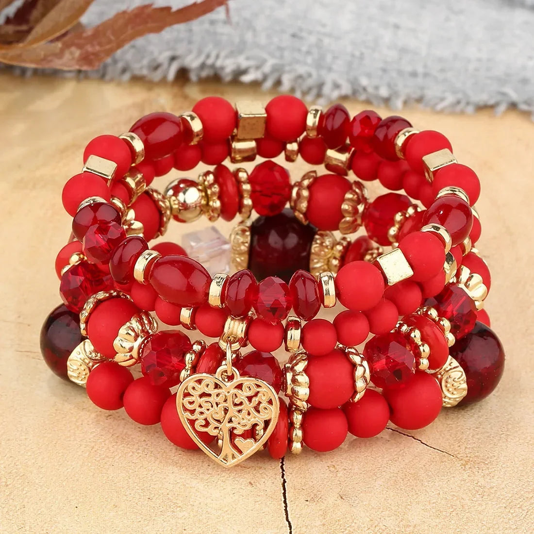 Stack of red beaded bracelets with gold accents and a heart charm on a textured surface.