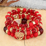 Stack of red beaded bracelets with gold accents and a heart charm on a textured surface.
