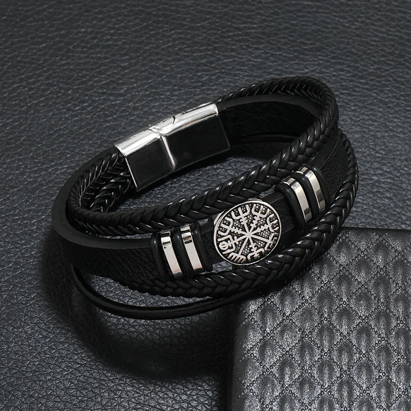 Black braided leather bracelet with metal clasp and emblem on a textured gray surface