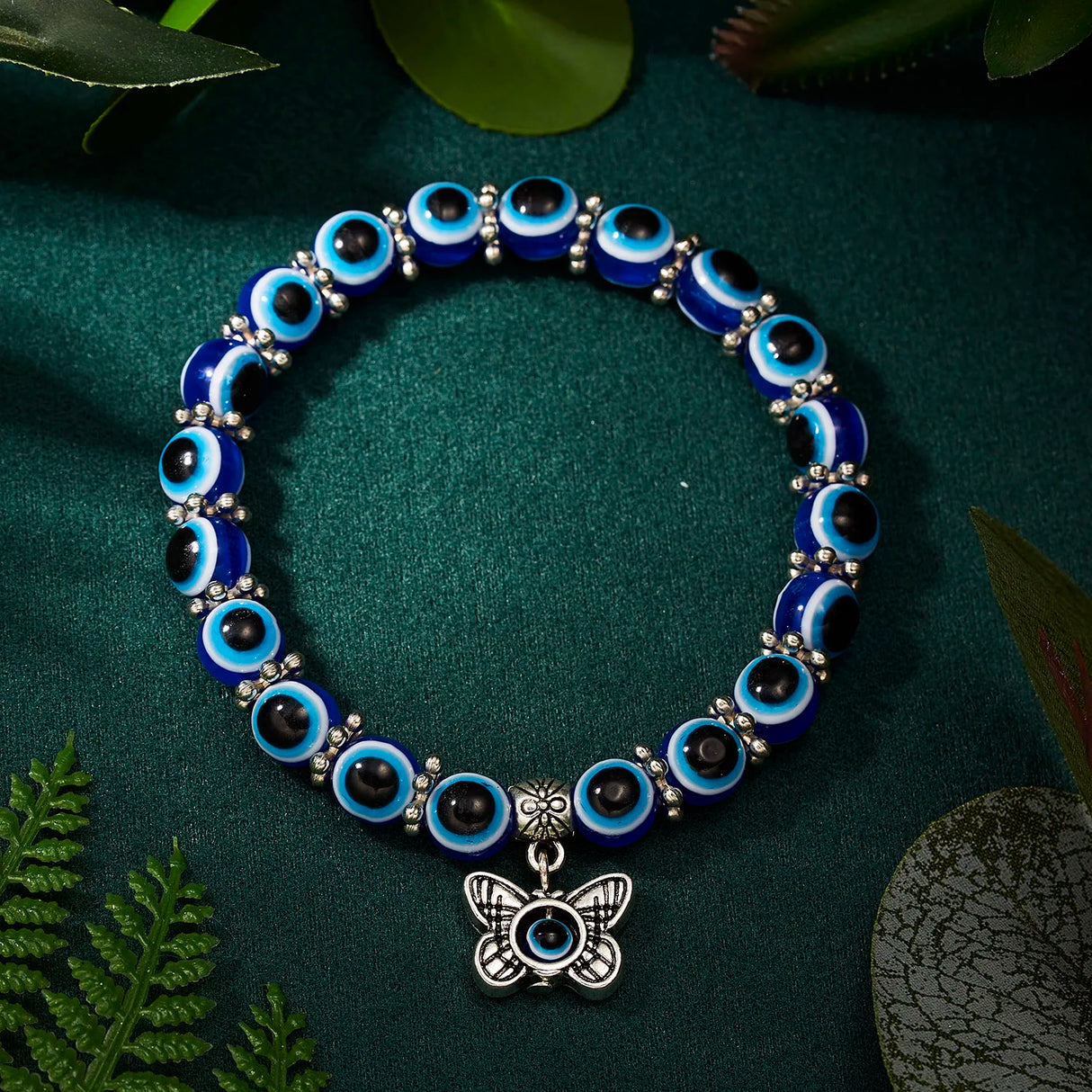 Blue beaded bracelet with a silver butterfly charm on a green fabric background