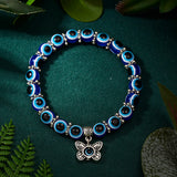 Blue beaded bracelet with a silver butterfly charm on a green fabric background