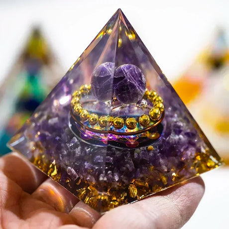 Pyramid-shaped crystal with purple stones and gold accents held by a hand.