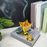 Gold incense burner with smoke on a book with plant and books in the background