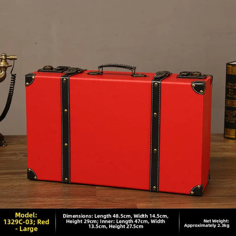 Red suitcase with black accents on a wooden surface against a gray wall.