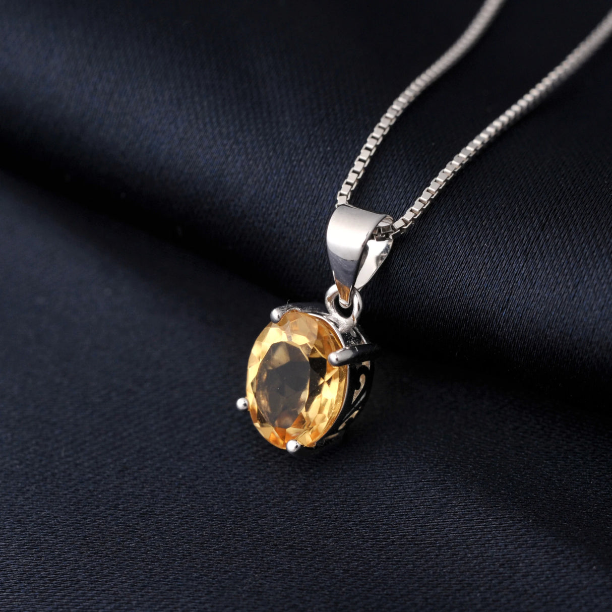 Silver pendant with a yellow gemstone on a dark fabric background