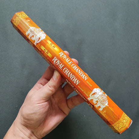 Hand holding a box of Royal Chandan incense sticks against a dark background