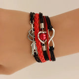 Bracelet with heart, arrow, and infinity symbols on a wrist against a neutral background