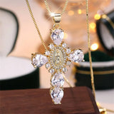 Gold cross necklace with clear gemstones on a wooden surface