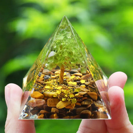 Pyramid-shaped crystal with embedded stones and a greenish tint held by a hand against a blurred green background