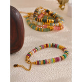 Colorful beaded bracelet with gold chain on a textured surface