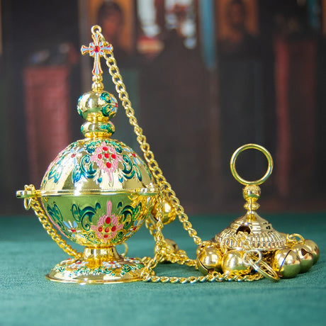Decorative gold and green egg-shaped object with chain on a teal surface