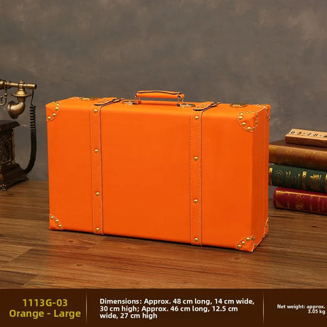 Orange suitcase on a wooden surface with books and a vintage phone in the background