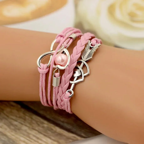Pink leather bracelet with silver charms on a wrist, blurred background