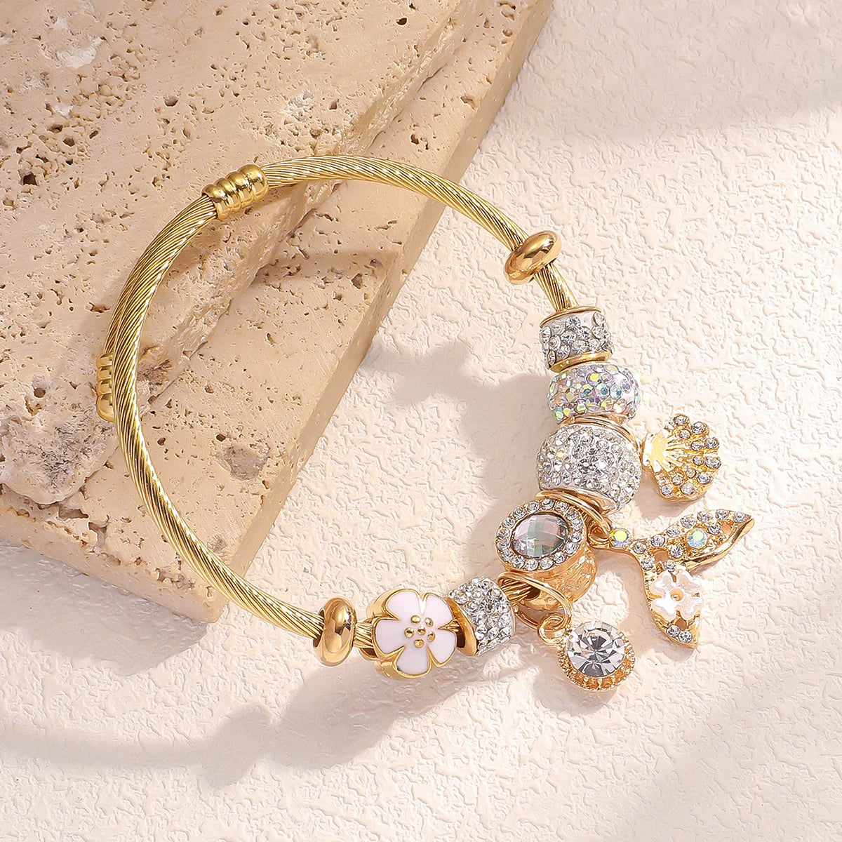 Gold bracelet with various charms on a textured beige surface