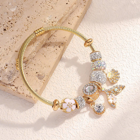 Gold bracelet with various charms on a textured beige surface