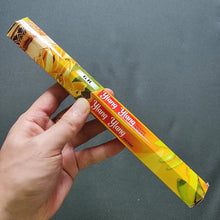 Hand holding a box of Ylang Ylang incense sticks against a gray background