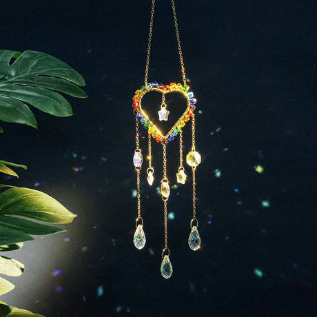 Decorative hanging heart-shaped ornament with colorful beads and teardrop shapes against a dark background.
