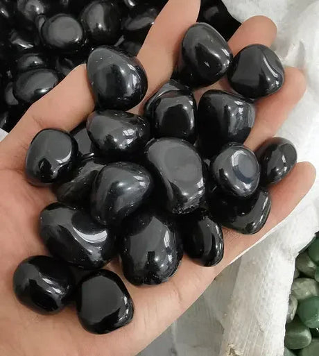 Hand holding a collection of glossy black stones with a blurred background