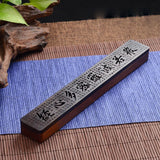 Long rectangular object with engraved text on a blue mat with natural elements