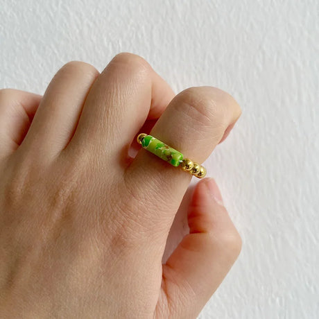 Hand wearing a gold ring with green stones against a white background
