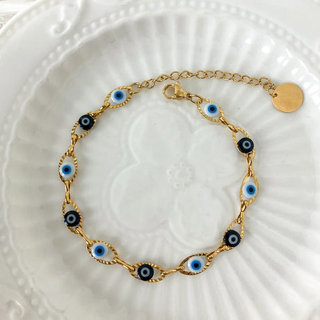 Gold bracelet with blue and black eye-shaped charms on a white textured plate