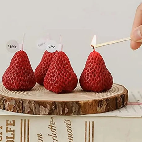 Red pear-shaped candles on a wooden base with a hand lighting one of them.