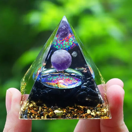 Triangular crystal pyramid held in hand with a colorful interior against a green blurred background