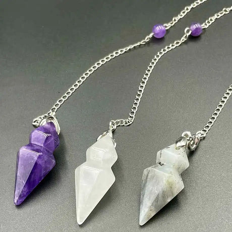 Three crystal pendants on silver chains against a gray background