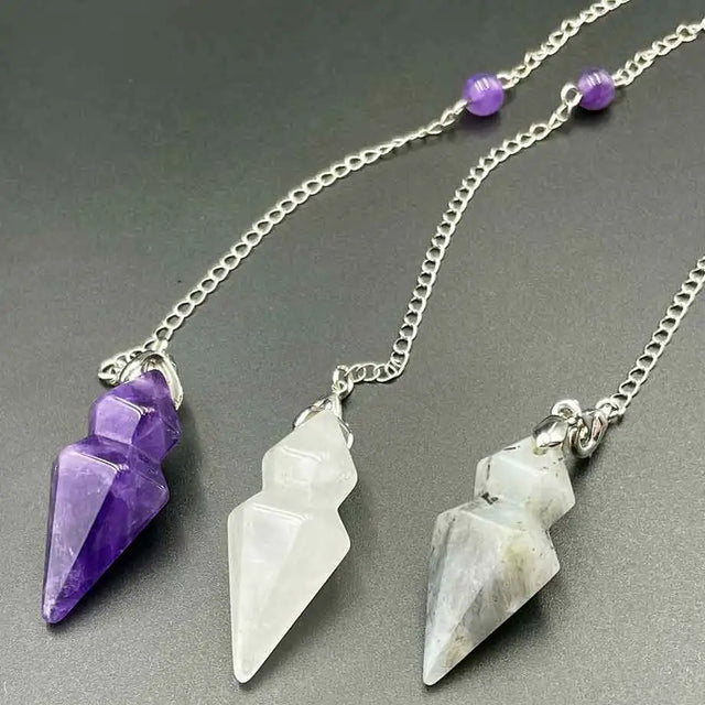 Three crystal pendants on silver chains against a gray background