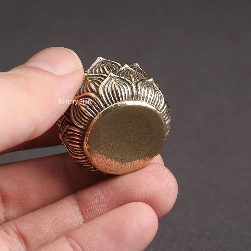 Hand holding a decorative bronze object with intricate design against a dark background