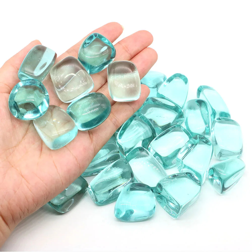 Hand holding turquoise glass pebbles with more pebbles on a white background